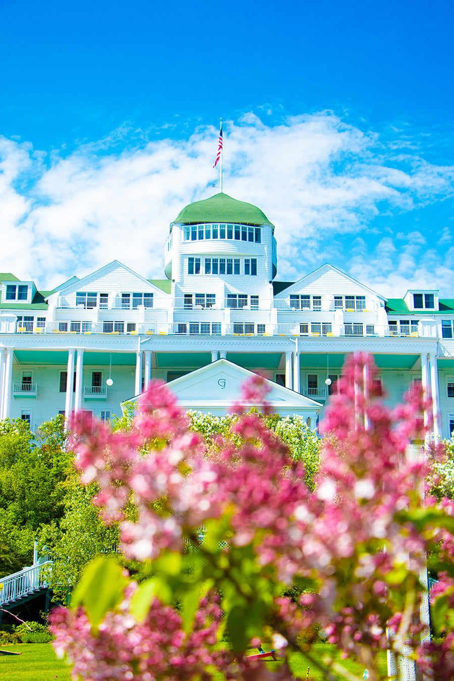 Lilacs & Grand Hotel's Cupola by Jennifer Wohletz. Photography on canvas mounted on black styrene. 10" x 15" Description: Lilacs bloom in the Tea Garden beneath the Grand Hotel. An American flag waves above the hotels cupola.