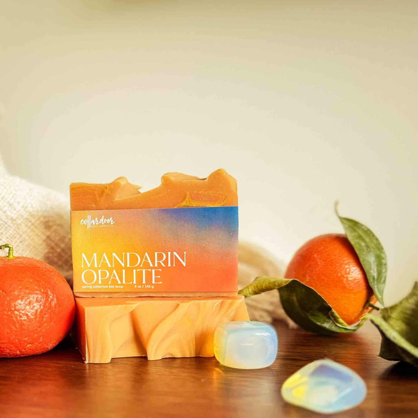 Bar of soap with Mandarin Opalite packaging, mandarin oranges, and opalite stones on a wooden surface.