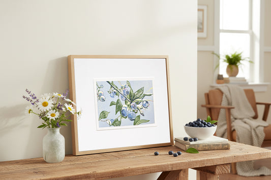 Framed blueberry block print on a wooden table with a vase of flowers and a bowl of berries.