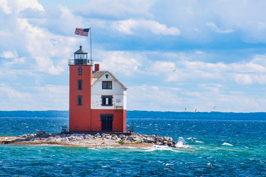 The USA flag flies over Round Island Lighthouse across the channel from Mackinac Island.&nbsp; The lighthouse serves as the finish line for sailing races starting from Chicago and Bayview Yacht Clubs each summer.