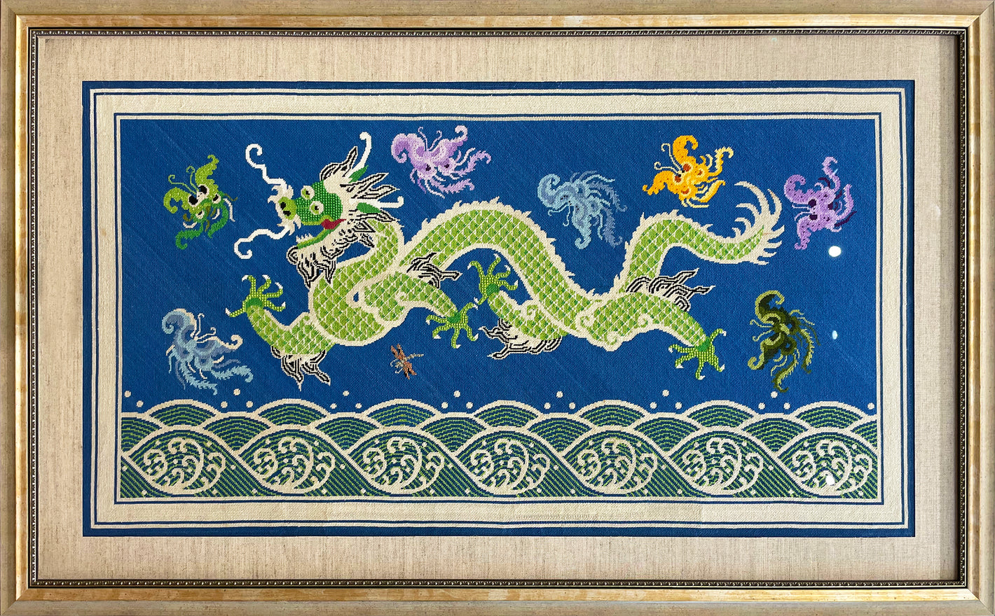 Large needlepoint of a dragon and fantastical creatures over a rolling sea framed in a gold frame with a black and gold fillet.
