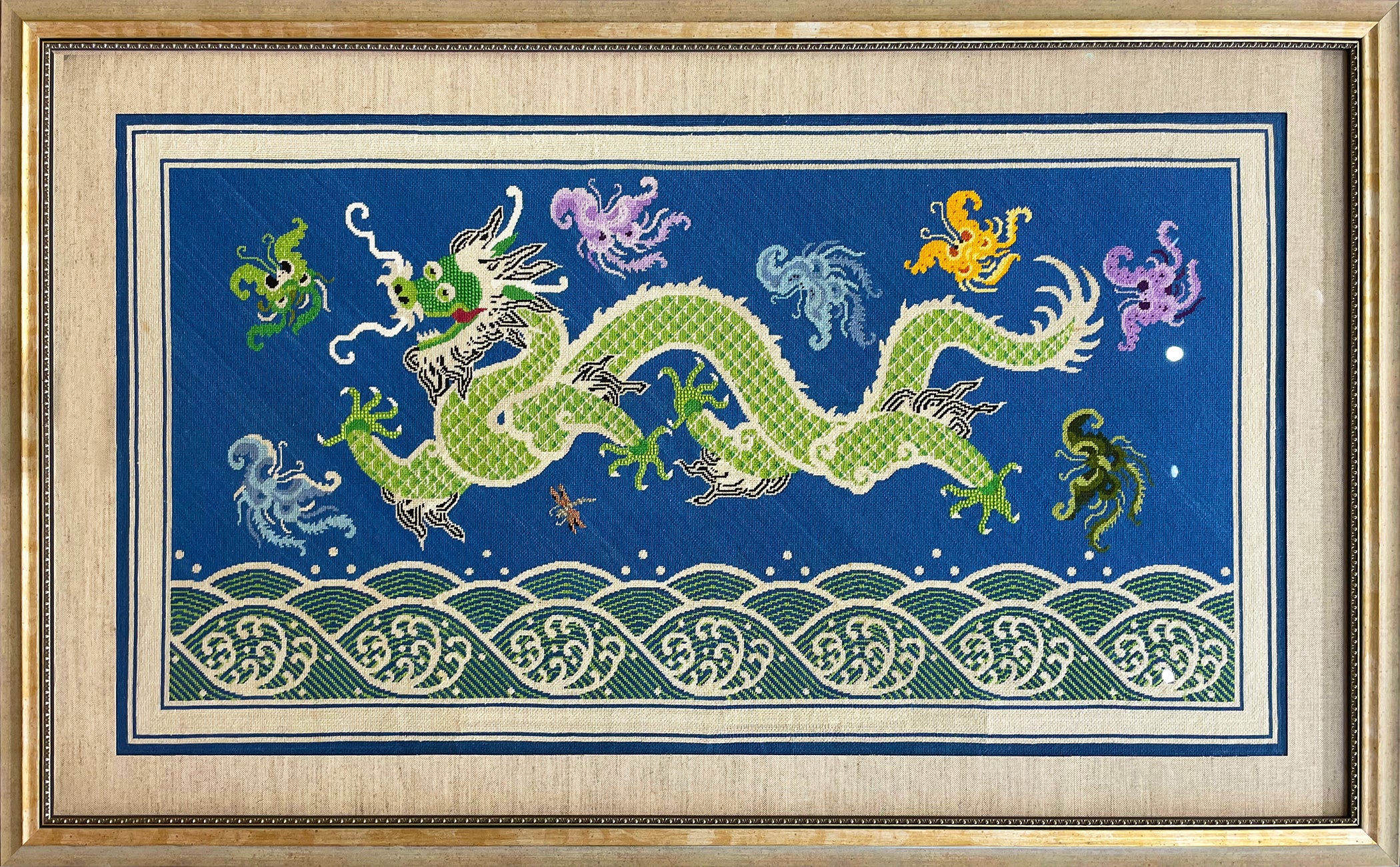 Large needlepoint of a dragon and fantastical creatures over a rolling sea framed in a gold frame with a black and gold fillet.