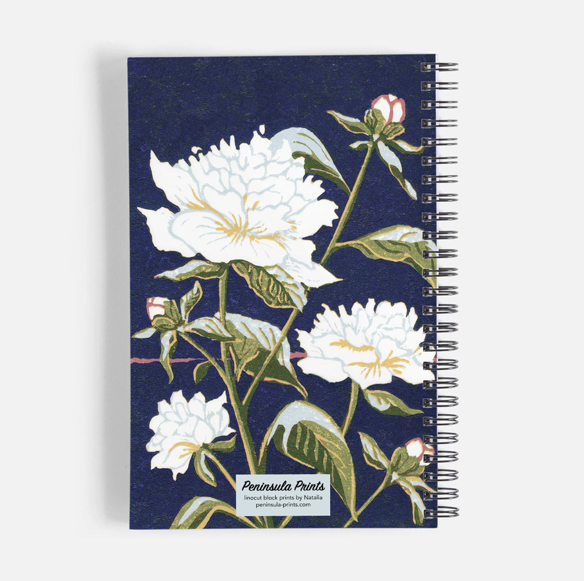 A spiral-bound notebook with a navy blue cover featuring a botanical block print of white peonies and green leave by Natalia Wohletz of Peninsula Prints.